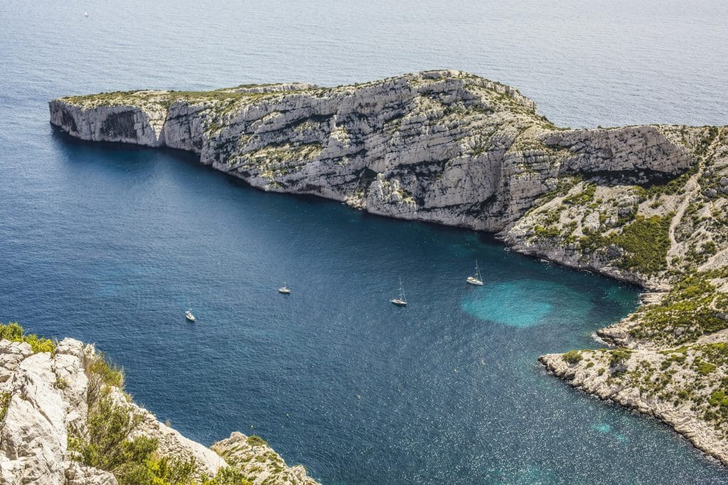 A breathtaking view of sailboats in a deep blue bay surrounded by rugged limestone cliffs.