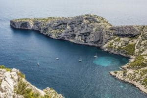A breathtaking view of sailboats in a deep blue bay surrounded by rugged limestone cliffs.