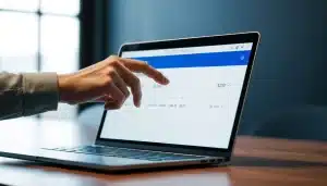 Main validant un virement bancaire sur un ordinateur portable dans un bureau sombre